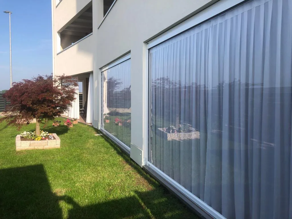 Chiusura di veranda con teli trasparenti e tende verticali su vetrata