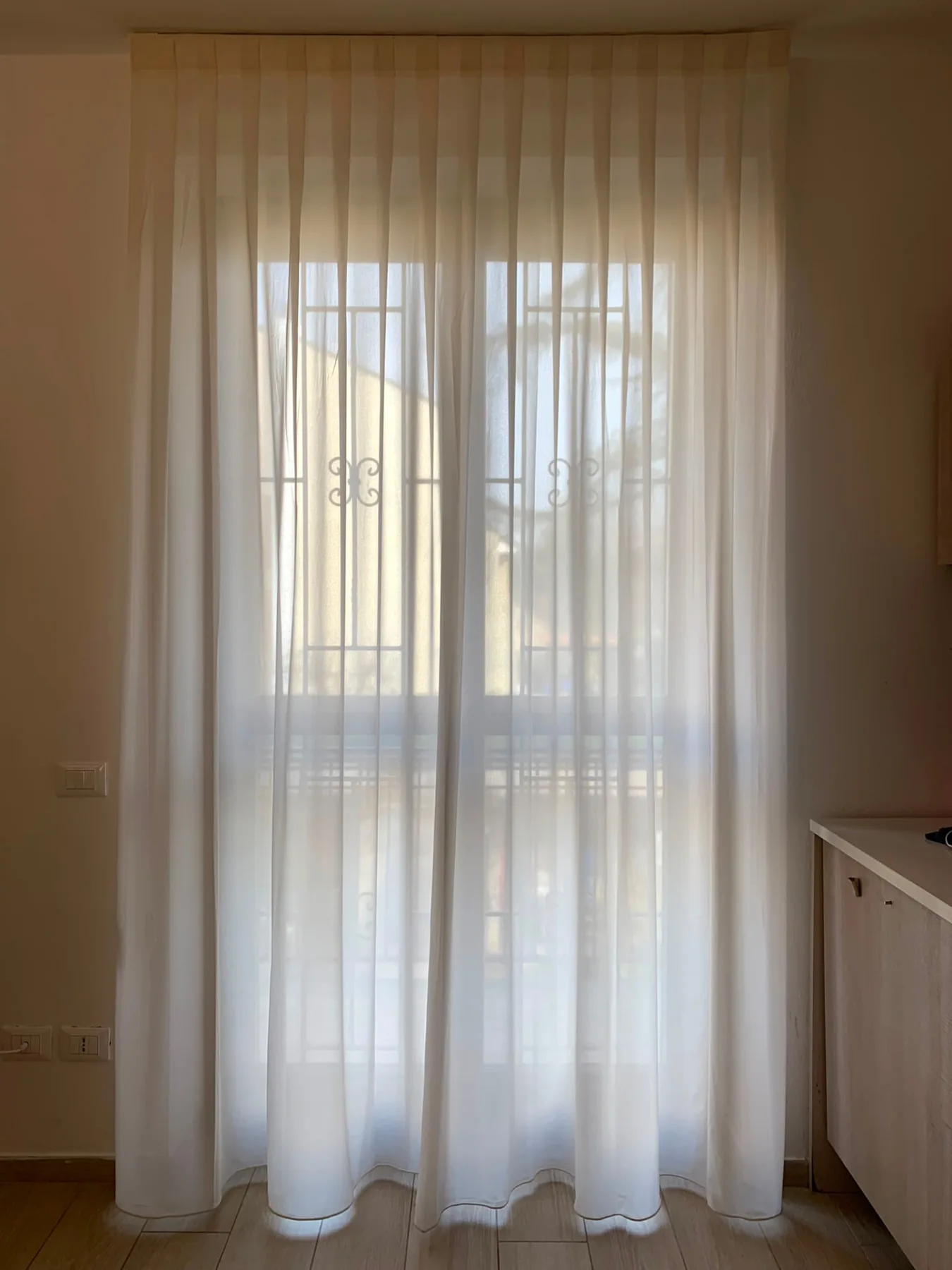 Tenda in velo bianco a pieghe su portafinestra controluce